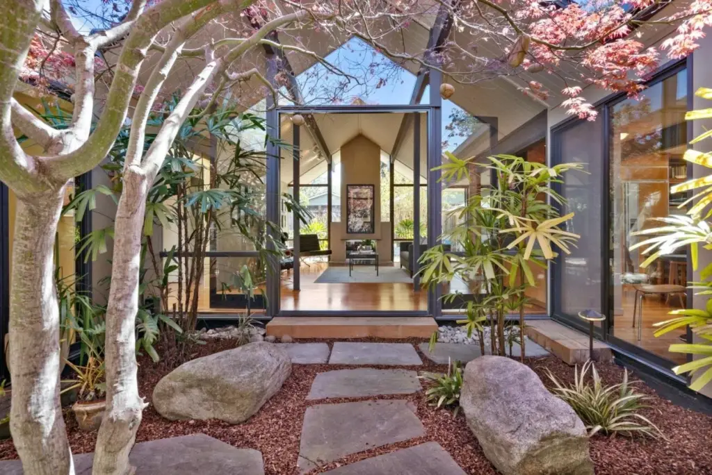 Modern Eichler home courtyard with exposed beams, floor-to-ceiling glass windows, and natural landscaping